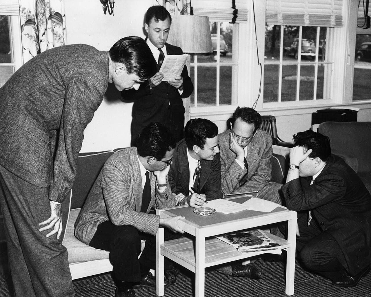 Richard Feynman and colleagues collaborating over papers at a table